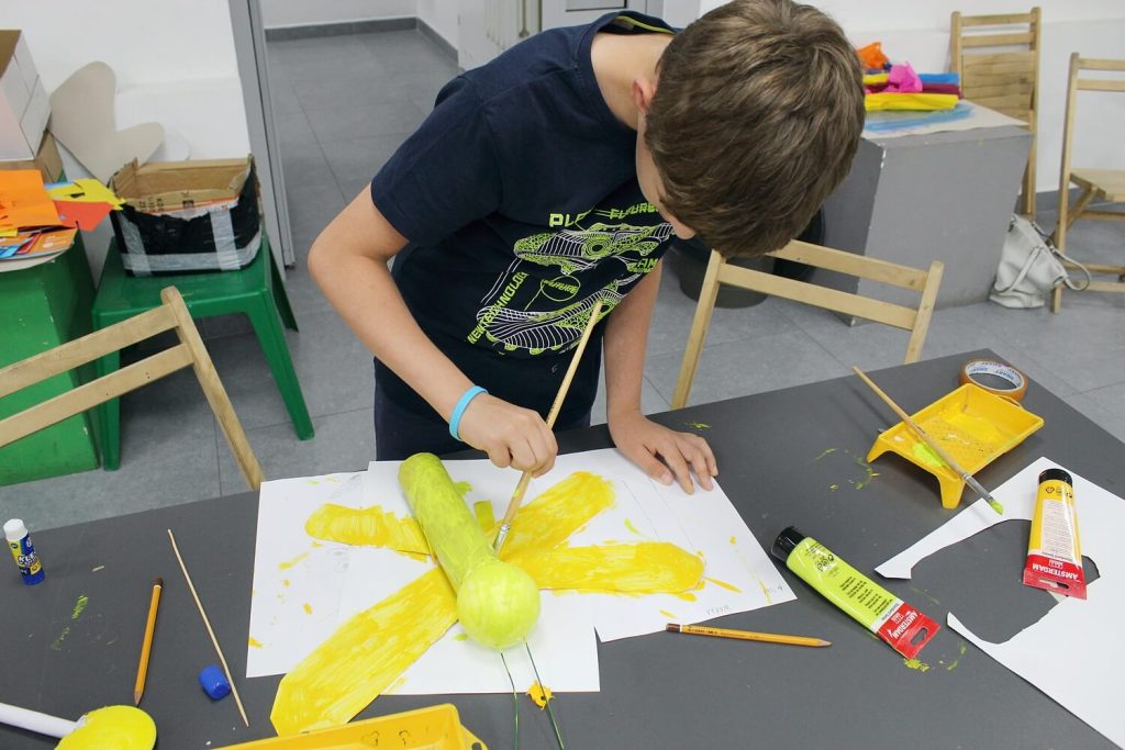 Chłopiec maluje na żółto swoją pracę