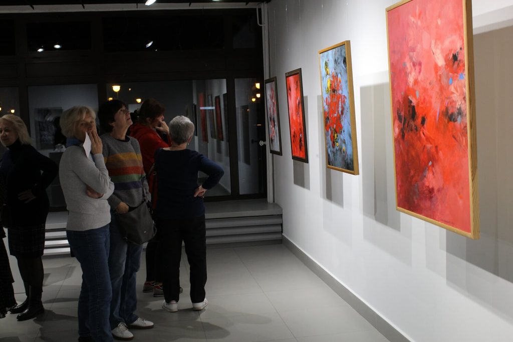 Zwiedzający wystawę oglądające serię obrazów w ramach wystawy Trzy Światy