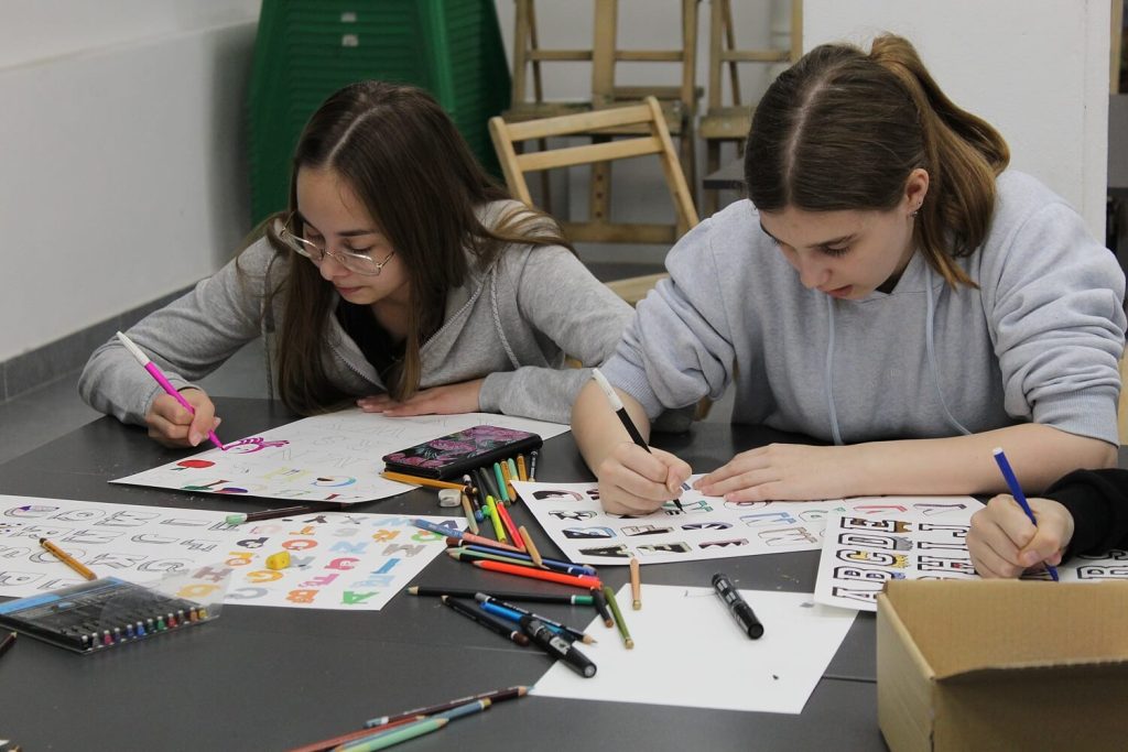 Dwie dziewczynki w trakcie warsztatu malują litery alfabetu