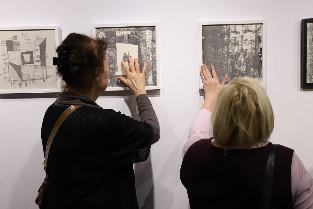 Kobiety dotykające powieszonych na ścianie dzieł Laury Dyczko