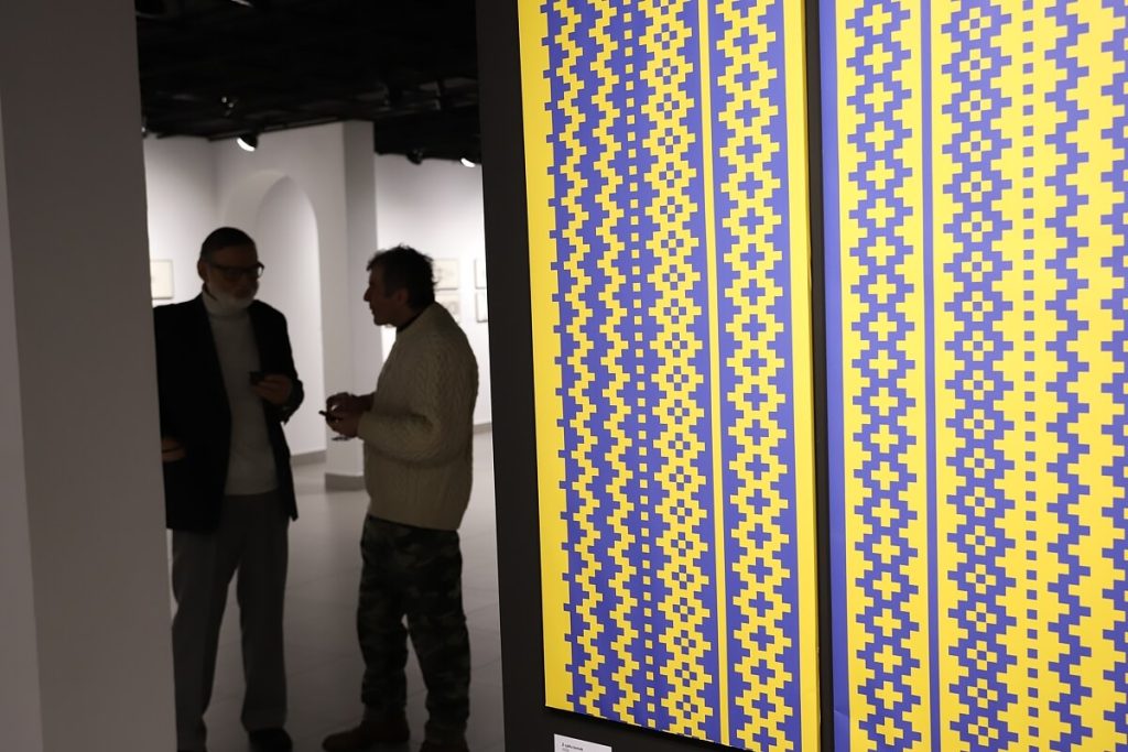 Na pierwszym planie dzieło Laury Dyczko w tle dwóch mężczyzn rozmawiających w trakcie wystawy