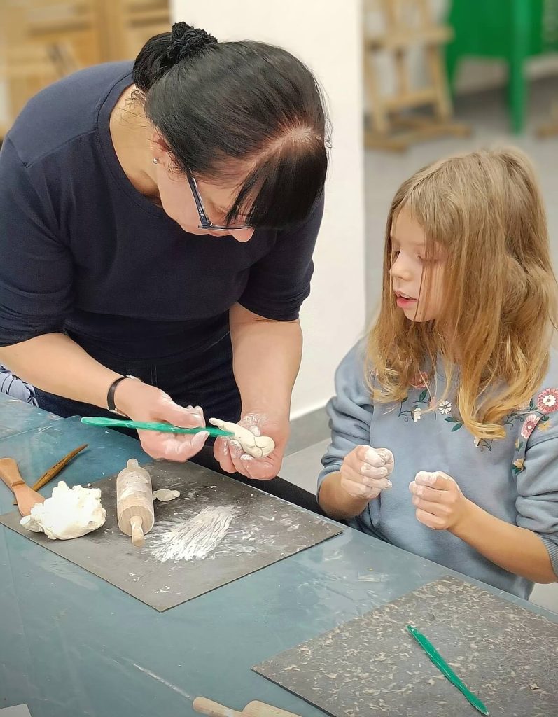 Prowadząca pokazuje dziewczynce jak rzeźbić w glinie