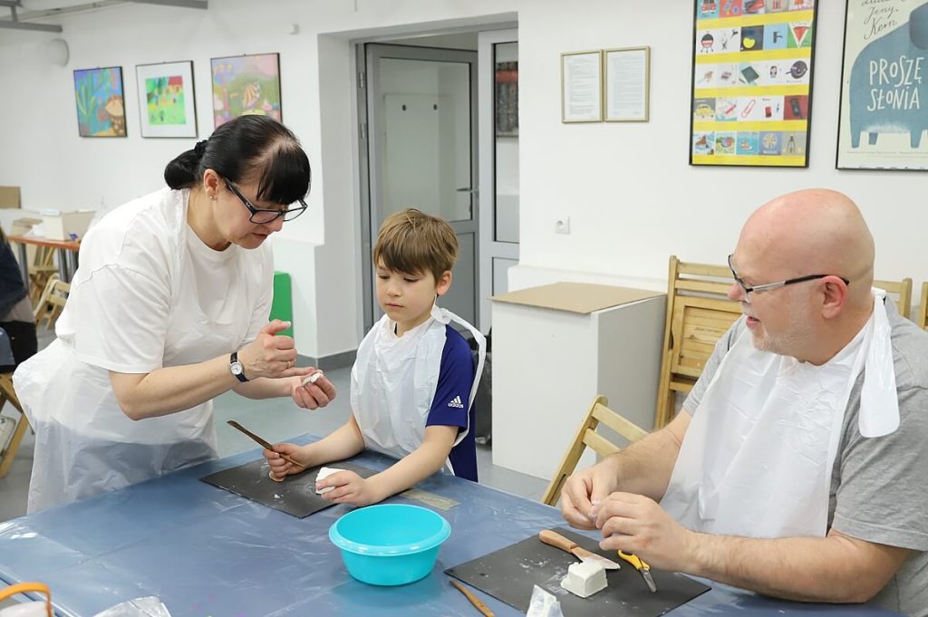 Prowadząca warsztaty dająca instrukcję chłopcu jak rzeźbić w glinie