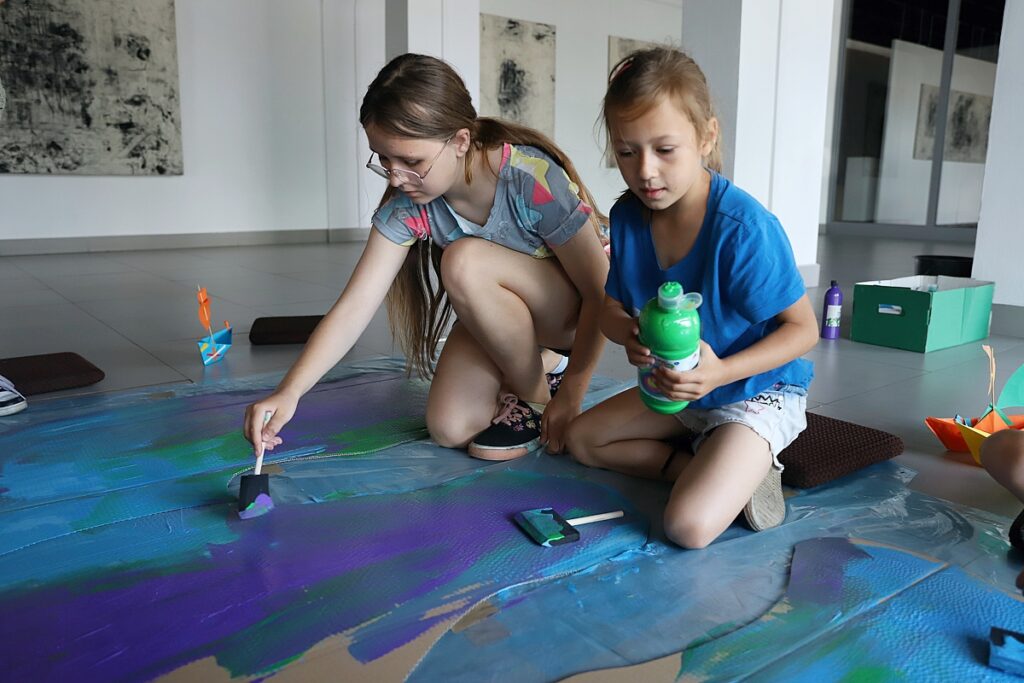 dziewczynki malują farbami arkusz kartonu