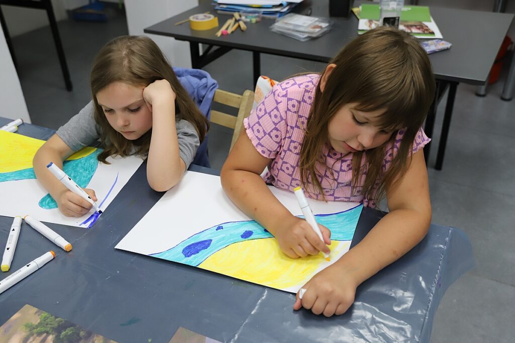 Dziewczynki rysują flamastrami pejzaż z rzeka
