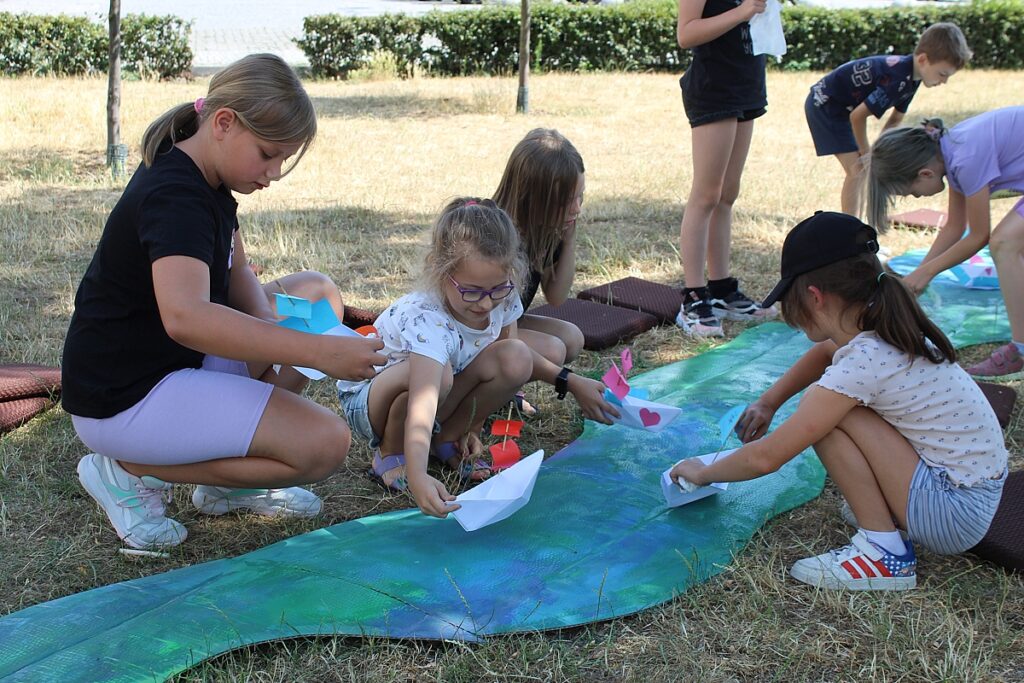 Dzieci ustawiają papierowe łódki na rzece