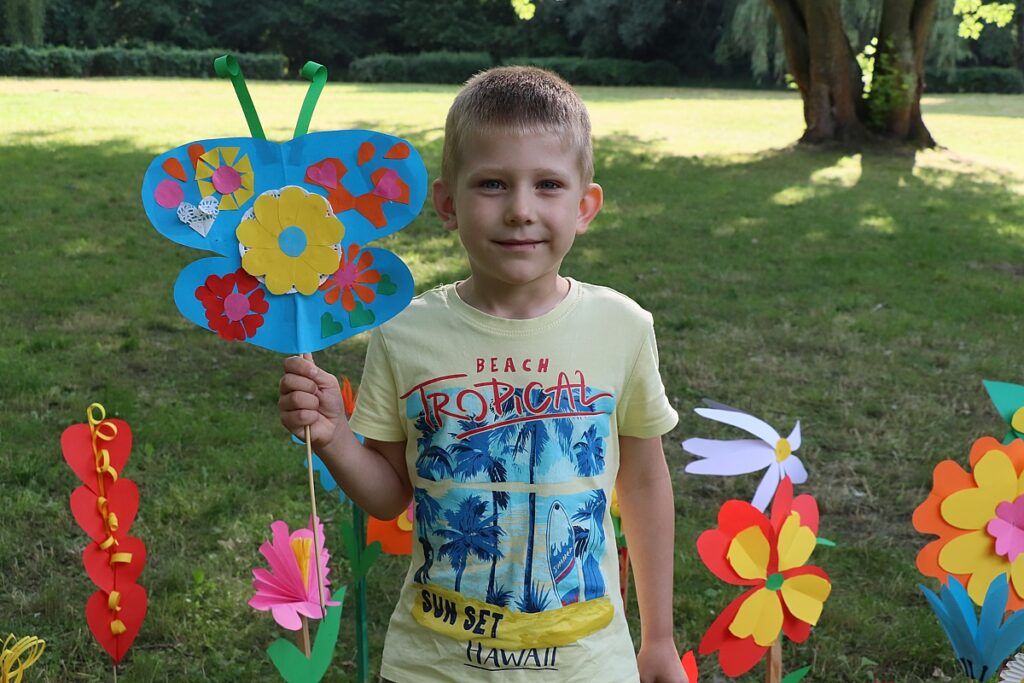 Chłopiec stoi na tle łąki w ręku trzyma kolorowego papierowego motyla